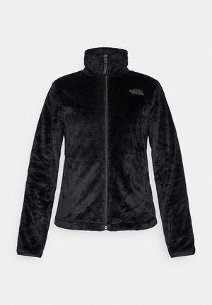 Chaqueta de forro polar negra con cuello alto, cierre de cremallera completo y mangas largas. Presenta una textura suave y un pequeño logo en el pecho.