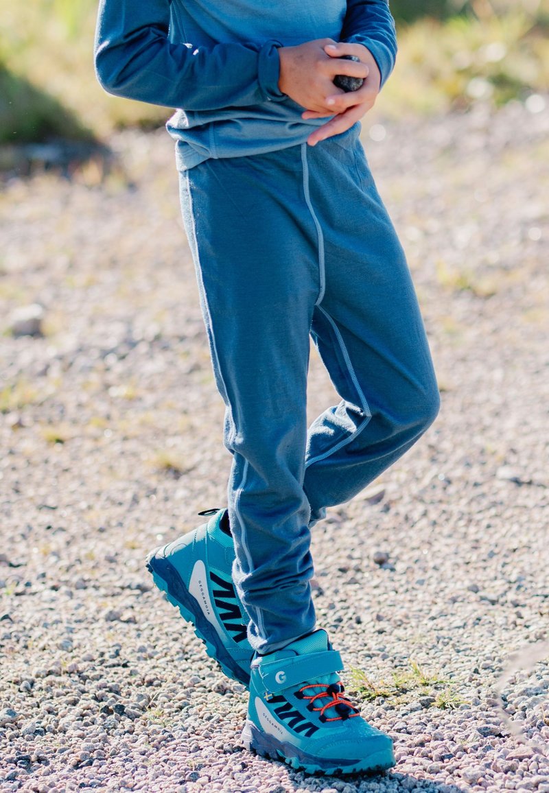 Blå langærmet skjorte og matchende bukser lavet af blødt materiale. Lyseblå vandrestøvler med sorte accenter og orange snørebånd. Udeliv.