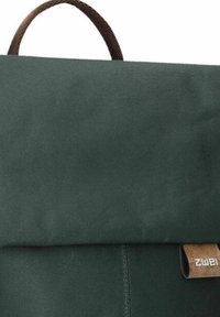 Mochila de tela verde con una solapa plegable y detalles en cuero marrón. Cuenta con un asa superior y costuras visibles. Diseño simple y moderno.