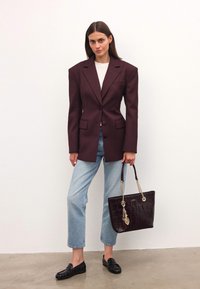 Bordeaux oversized blazer med skarpa axlar, framfickor; ljusgrå topp, blå cropped jeans; mörkbrun tote-väska med kedja och tofs.