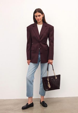 Bordeaux oversized blazer met scherpe schouders, voorzakken; lichtgrijze top, blauwe cropped jeans; donkerbruine tote bag met ketting en kwastje.