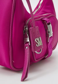 Borsa a mano in nylon rosa con hardware argentato. Include una maniglia in pelle testurizzata e un'etichetta con logo. Presenta una chiusura con zip e scomparti organizzati.