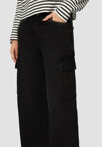 Jean cargo noirs en denim, dotés de poches latérales, d'une coupe décontractée et de détails de couture visibles. Associés à un haut à rayures à manches longues.