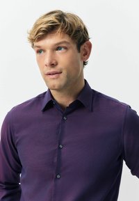 Koszula z długim rękawem w głębokim purpurowym kolorze, z subtelną teksturą, z kołnierzykiem w kształcie spiczastym i czarnymi guzikami z przodu.