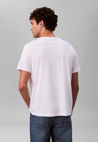 Bijela majica kratkih rukava s okruglim izrezom, glatke teksture i ravnim rubom. Nošena s plavim trapericama.