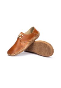 Zapatos de cuero marrón con un perfil bajo, cordones de cuero y un detalle de borde tejido. La suela presenta una marca grabada.
