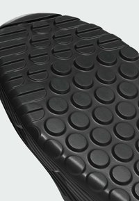 Sort gummisål til sko med en tekstureret overflade, der har runde forhøjede prikker og riller for greb. Holdbar og designet til at give trækkraft.