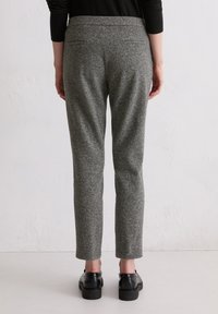 Graue, strukturierte Hose mit schmalem Schnitt, mittelhoher Taille und zwei Gesäßtaschen. Kombiniert mit schwarzen Lederschuhen.