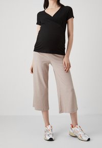 Haut enveloppant noir à rayures avec des manches courtes, associé à des culottes beige à rayures. Chaussures : baskets de sport blanches et orange.