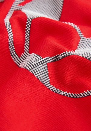 Červená látka s texturovaným vzorem tvořeným bílými a černými vystouplými prvky; hladká textura s kontrastními designovými prvky.