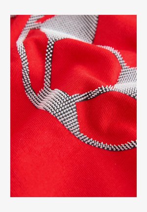 Rdeča tkanina z vzorcem teksture, oblikovanim iz belih in črnih reliefnih elementov; gladka tekstura s kontrastnimi oblikovalskimi detajli.