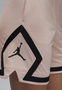 Pantalones cortos deportivos rosas con un acabado texturizado, con el logo negro de Jumpman y detalles angulares negros a lo largo del dobladillo.