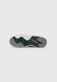 Lacoste sneaker sole in black, white, and grey. Features textured rubber with zigzag patterns and red accents. Labeled 'LACOSTE.'