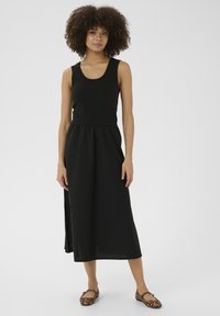 Svart midi-klänning med en ribbad topp, samlad midja och flödande tyg. Bärs med leopardmönstrade ballerinat. Slät, lätt textur.