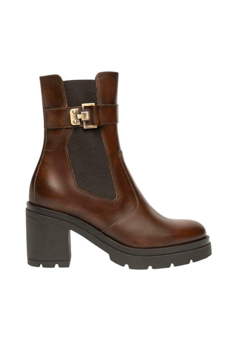 Stivale alla caviglia in pelle marrone con tacco a blocco, pannello laterale elastico nero e cinturino decorativo con fibbia dorata su sfondo bianco.