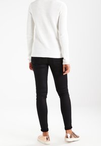 White knitted sweater with ribbed cuffs and hem, paired with black skinny jeans and metallic detailed sneakers. View from the back.