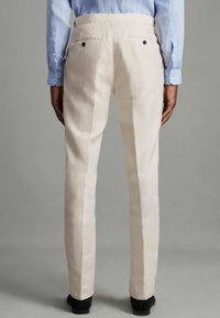Pantalons beige clair en tissu texturé, présentant une coupe droite, des poches arrière avec boutons foncés et une taille lisse.