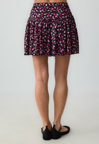 Schwarz geblümter Rock mit rosa und weißen Blumen, gerafftem Design und elastischem Bund. Leichter Stoff mit fließender Silhouette.