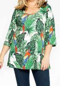Haut à imprimé floral avec des feuilles vertes et des perroquets rouges, bleus et jaunes vifs. Il dispose d'un décolleté arrondi et de manches trois-quarts.