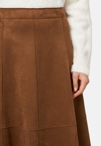 Barna színű, velúr anyagú A-vonalú szoknya látható varrásokkal, enyhén texturált felülettel és derékrésszel, deréktól lefelé bemutatva.