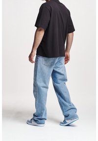 Svart bomullst-shirt, lös passform, kombinerad med ljusblå denimjeans. Skor är vita med blå accenter. Enkel design, inga synliga logotyper.