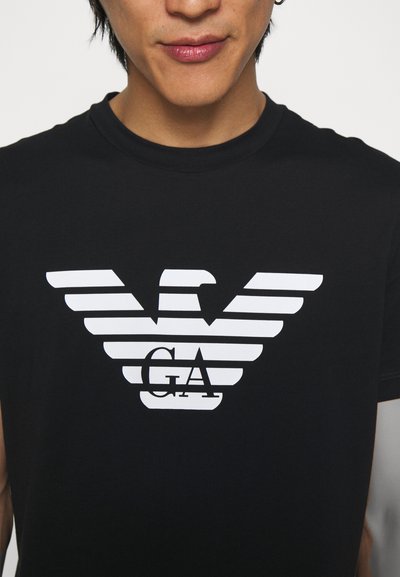 Black t-shirt featuring a white eagle logo with horizontal stripes and the letters "GA" integrated into the design.