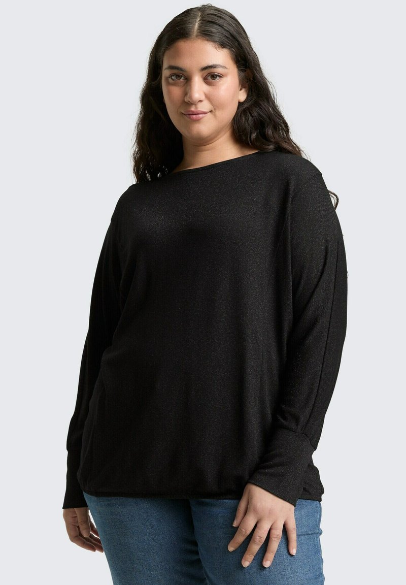 Zwarte lange mouwen shirt met een losse pasvorm, bootnek en geribde manchetten, gecombineerd met blauwe jeans. Zachte textuur met een subtiele glans.