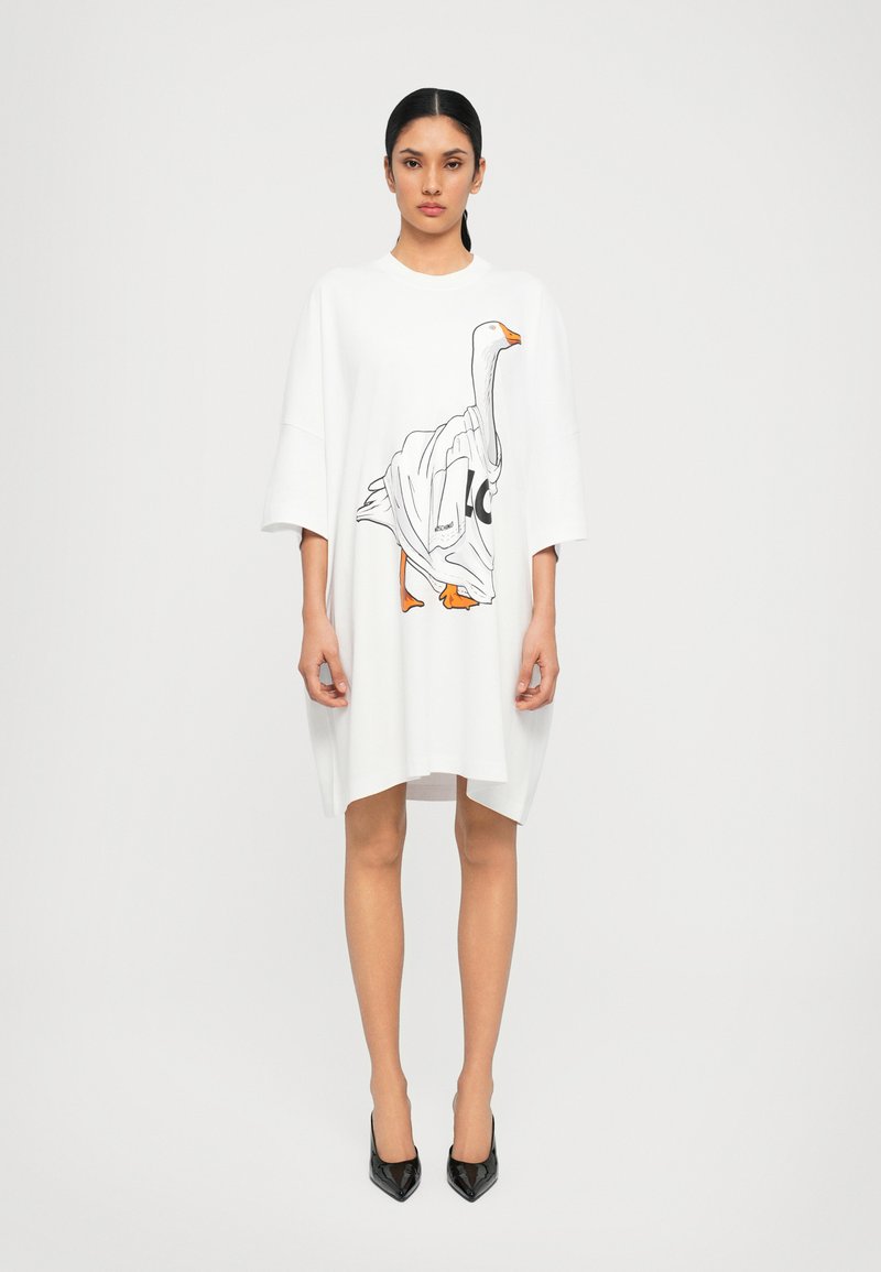 Robe à manches courtes surdimensionnée en coton blanc, ornée d'un motif de l'oie noir et orange à l'avant, avec un col rond et un ourlet asymétrique.