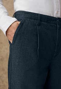 Dunkelgraue Hosen mit Fischgrätmuster aus strukturiertem Stoff, mit Taschen und normaler Passform, kombiniert mit einem weißen Hemd mit Kragen.