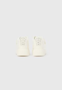 Ζευγάρι εκρού sneakers με πλατφόρμα, εμφανιζόμενα από πίσω με κυκλικές οπές στην περιοχή της φτέρνας, τοποθετημένα σε απλή φόντο.