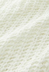 Bijeli pleteni materijal s teksturiranim otvorenim tkanjem, koji sadrži mekane, fleksibilne niti i lagan, prozračan izgled.