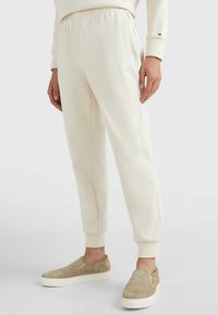 Joggers de color crema, hechos de una tela suave, con un logotipo en relieve a lo largo del costado y una cintura elástica para mayor comodidad.