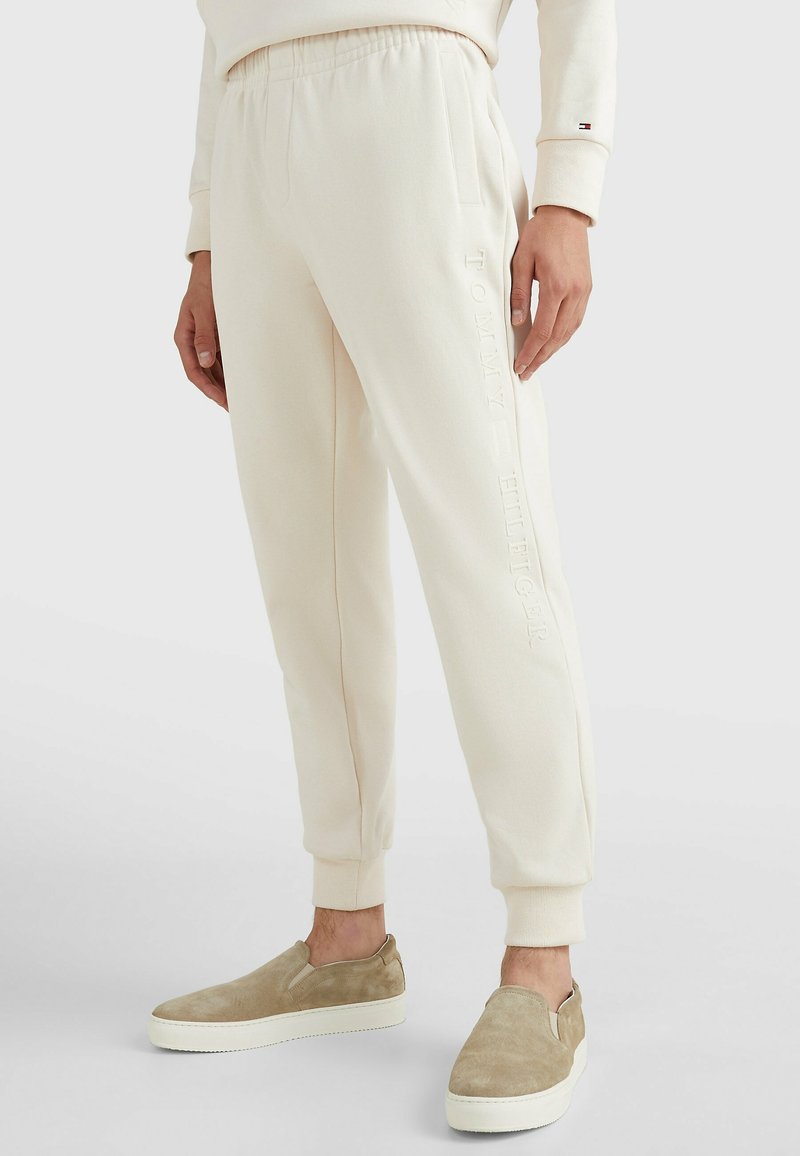 Joggers de color crema, hechos de una tela suave, con un logotipo en relieve a lo largo del costado y una cintura elástica para mayor comodidad.