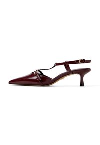 Burgundy lakan nahkaa slingback-kenkä, jossa on terävä kärki, T-hihnan muotoilu, koristeellinen kultainen yksityiskohta ja matala, lievästi levenevä korko.