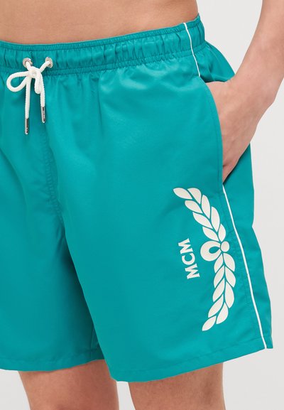 Pantaloni scurți de înot turcoaz cu garnitură albă pe laterale și un logo MCM, dotati cu un șnur la talie și un buzunar lateral. Realizați dintr-un material neted și ușor.