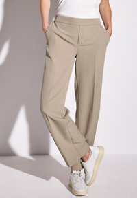 Beige, wijde broek met een gladde textuur, zijzakken en een platte tailleband, gecombineerd met witte sneakers.
