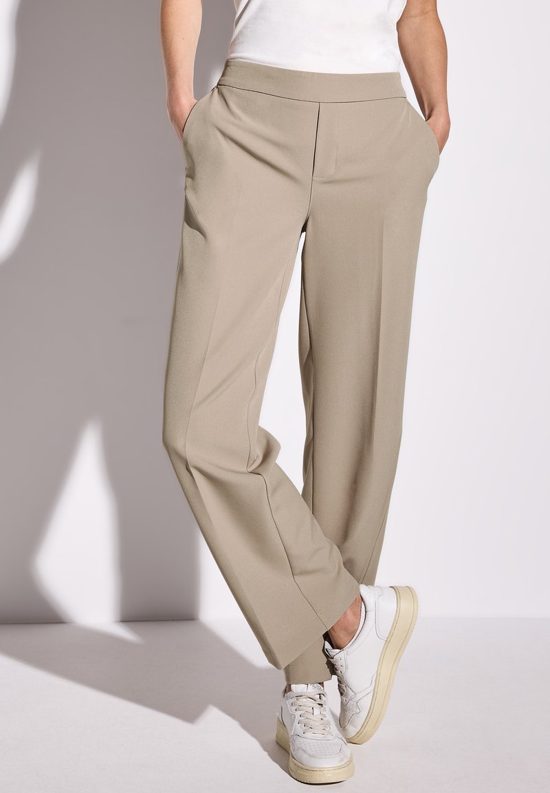 Beige, wijde broek met een gladde textuur, zijzakken en een platte tailleband, gecombineerd met witte sneakers.