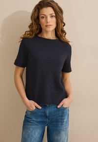 Haut bleu marine à manches courtes texturé avec un col rond, associé à un jean bleu clair ample avec des poches avant.