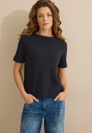 Haut bleu marine à manches courtes texturé avec un col rond, associé à un jean bleu clair ample avec des poches avant.