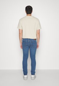 Camisa beige de manga corta y vaqueros ajustados azul oscuro con detalles de costuras sutiles y textura suave, complementado con zapatillas blancas.