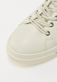 Weiße Leder-Sneaker mit abgerundetem Zehenbereich, strukturiertem Gummisol, Metallösen und flachen Schnürsenkeln. Glatte Oberfläche und minimale Designdetails.
