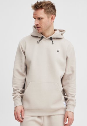 Beige hoodie with adjustable drawstring, kangaroo pocket, ribbed cuffs, and small logo accent on the chest. Smooth fabric texture.