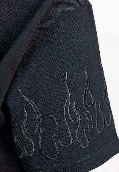 Maglietta nera a maniche corte con ricamo a forma di fiamma in una trama leggermente rialzata, posizionata nella parte inferiore della manica.