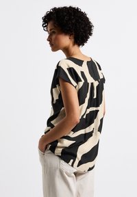 Top a maniche corte in beige e nero con motivo astratto; tessuto leggero, scollatura rotonda, dettagli plissettati sul retro, vestibilità rilassata.