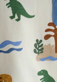 Grønne dinosaurer og styliserede planter samt blå bølger trykt på cremefarvet stof, der skaber et legende forhistorisk mønster.