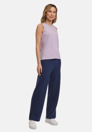Haut sans manches violet clair associé à un pantalon large navy, présentant une coupe décontractée et des fentes sur les côtés, porté avec des baskets blanches.