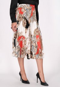 Faltenrock in einem mehrfarbigen Design mit Blumen- und Tiermotiven in Rot, Schwarz, Weiß und Goldtönen. Das Material wirkt leicht und fließend.
