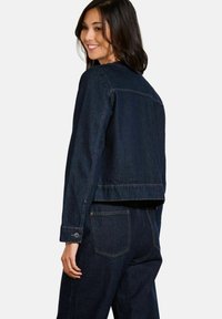 Veste en denim bleu foncé avec une coupe courte, des poignets à boutons, des poches avant et des détails de couture visibles sur les manches et le dos.