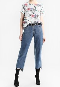 Floral-patterned white t-shirt with short sleeves, paired with high-waisted, straight-leg blue jeans featuring a raw hem and black belt.