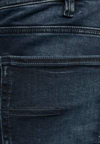 Donkerblauwe denim jeans met een achterzak met zichtbare stiksels en een gladde textuur. De stof heeft een lichte glans en reguliere stiksels.